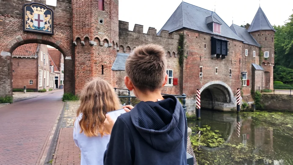 Twee kinderen van achteren gezien bij de Koppelpoort, het meisje met een telefoon in haar hand