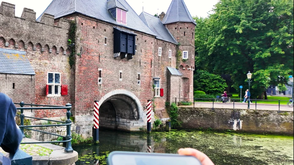 De Koppelpoort vanaf de overkant van het water, met onderin beeld een telefoon in iemands hand