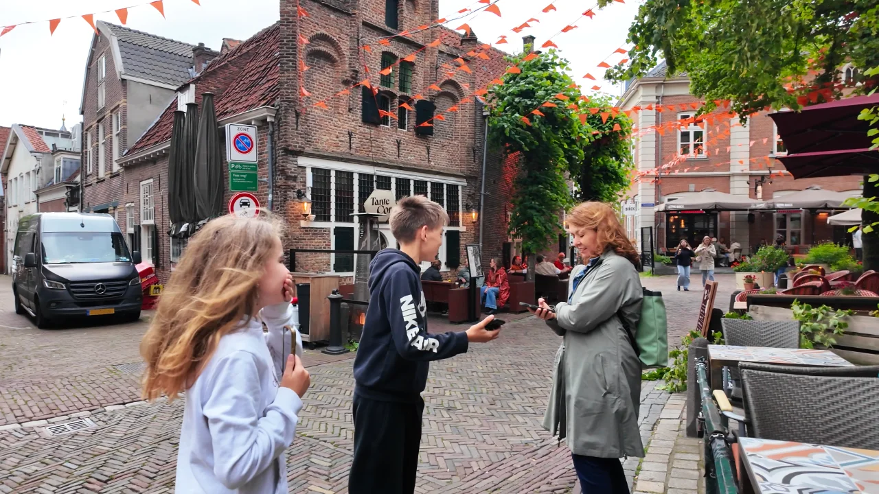 Een moeder en twee kinderen lachen in de oude binnenstad, ieder met een telefoon in de hand